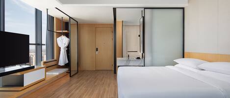 A modern hotel room with a large bed, a TV, a wardrobe, and a bathroom with a mirror.