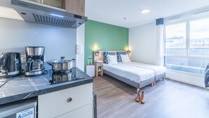 Una habitación de hotel moderna con una cama, una kitchenette pequeña, una ventana con vistas a la ciudad y un techo de madera.