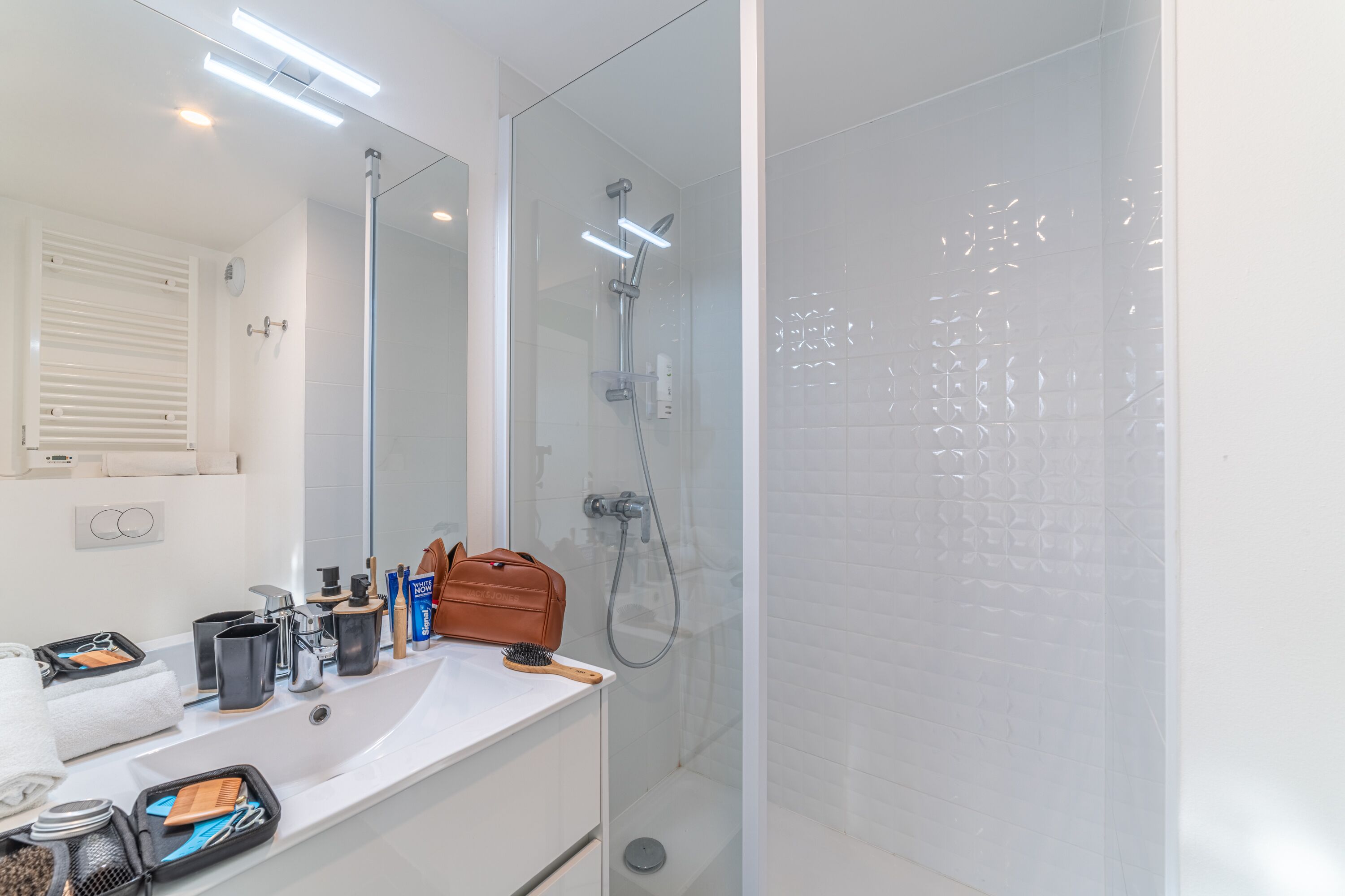 A modern bathroom with a glass-enclosed shower, a white sink with various toiletries, and a mirror above the sink.