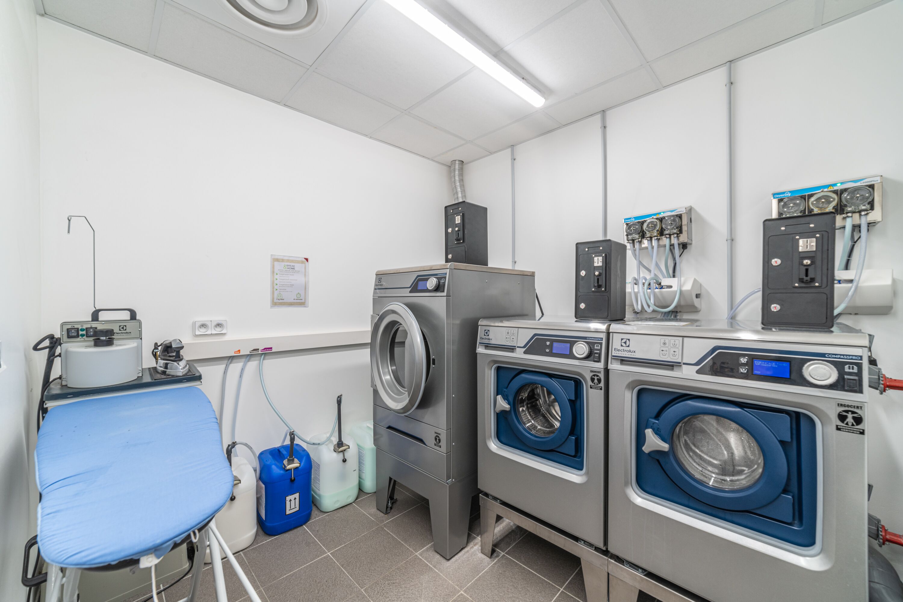 A laundry room with two front-loading washing machines, a drying machine, and a folding table with a blue cover.