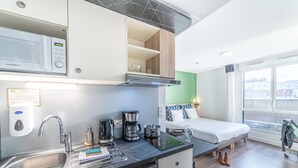Una cocina moderna con microondas, cafetera y lavabo. Hay una cama con vistas a la ciudad.