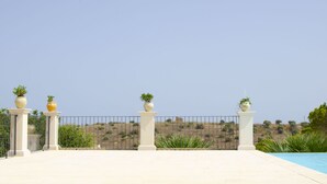 A pool area with a clear view of the surrounding landscape, including a fence and potted plants.