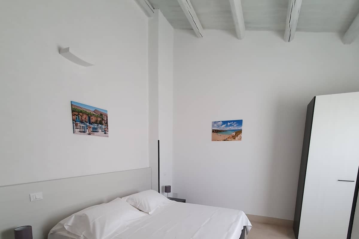 Un dormitorio con cama, mesita de noche, lámpara, armario y dos cuadros en la pared.
