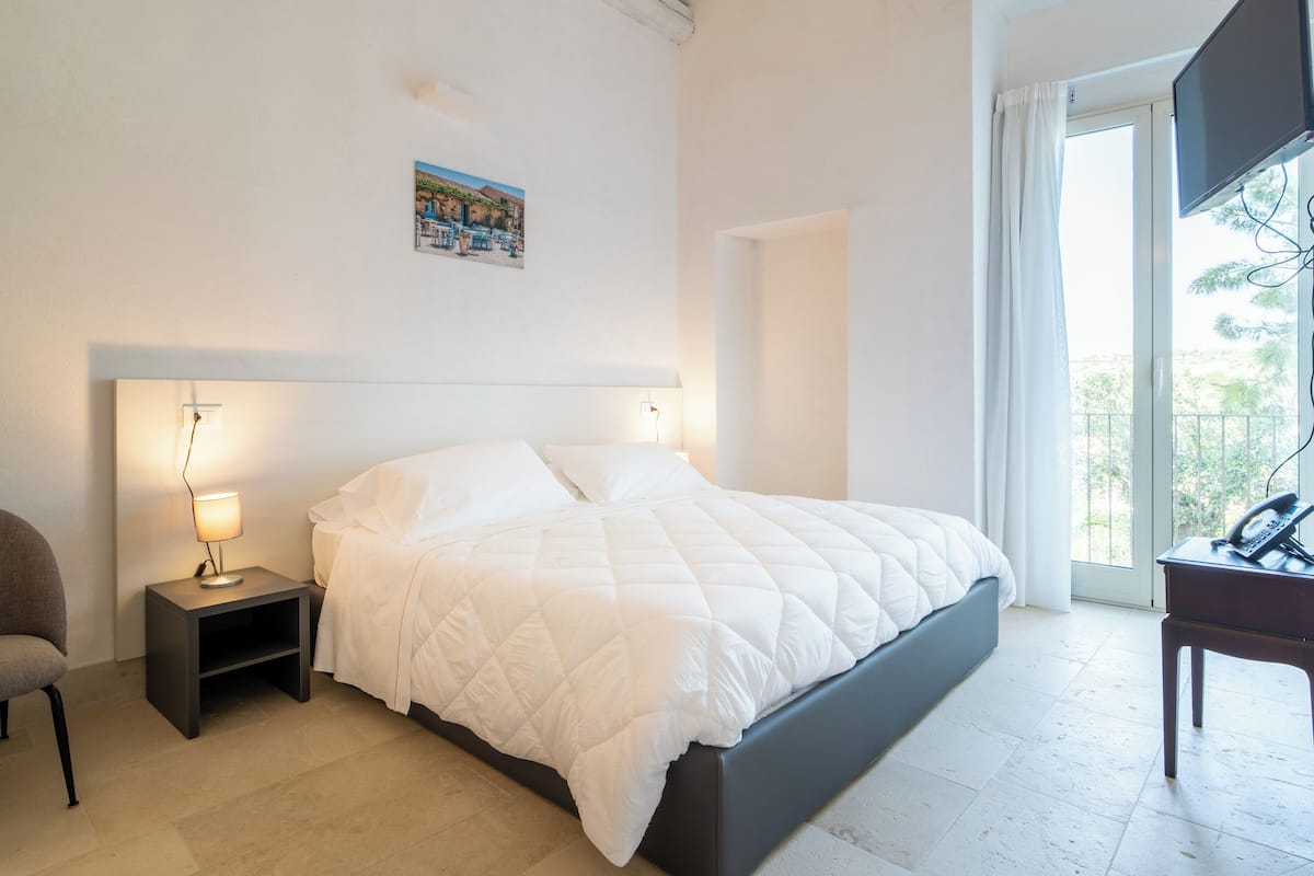 Un dormitorio con cama, mesitas de noche, una silla, un escritorio y ventana con vistas.