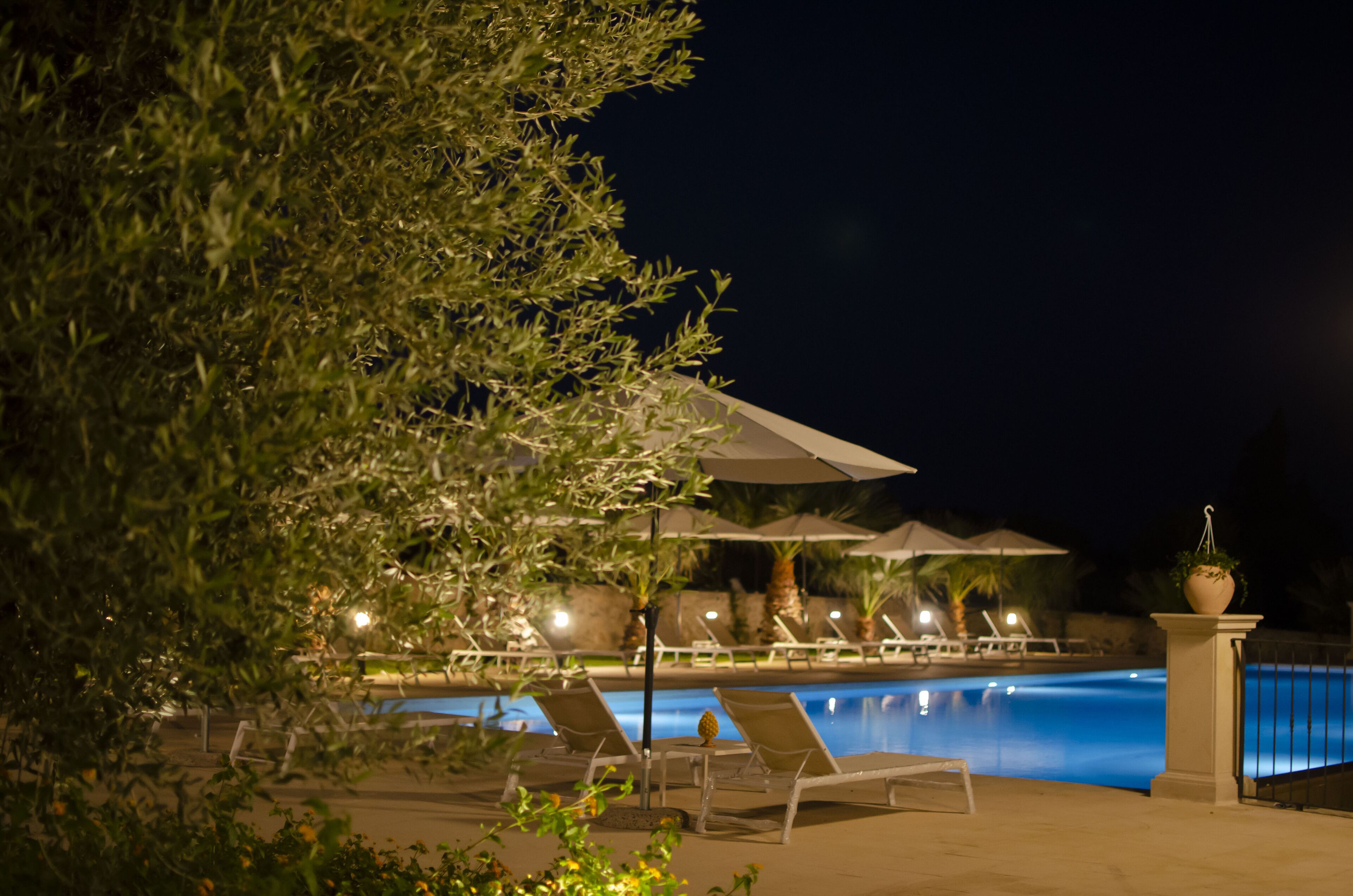 Un área de piscina nocturna con sillones de descanso y sombrillas.