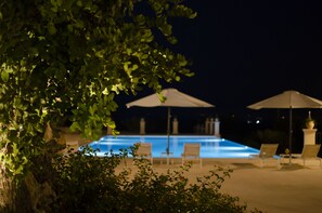 A nighttime swimming pool area with lounge chairs and umbrellas.