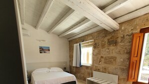 A bedroom with a bed, a bench, a window, and stone walls.
