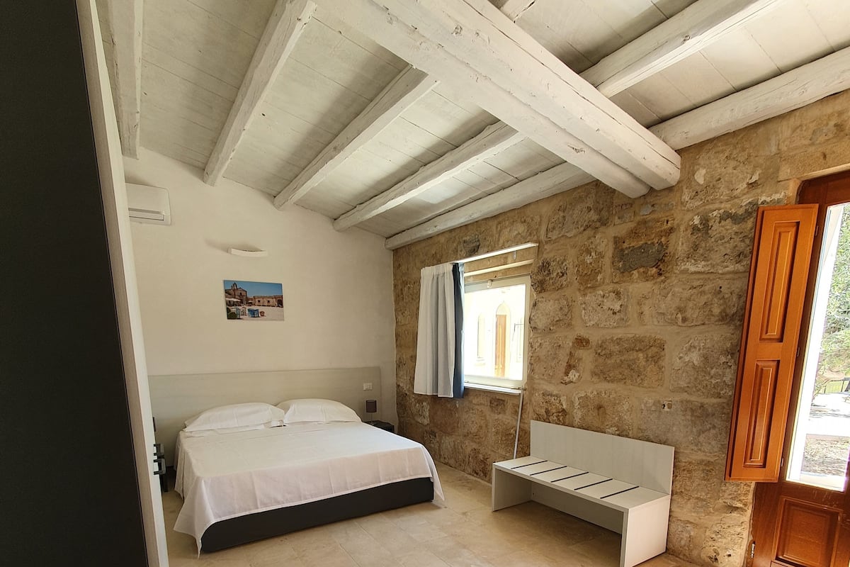 Un dormitorio con cama, un banco, una ventana y paredes de piedra.