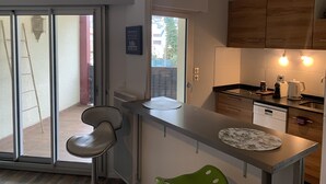 Une cuisine moderne dotée d’une porte-fenêtre coulissante donnant sur un balcon, d’un petit îlot central avec un évier et d’armoires en bois.