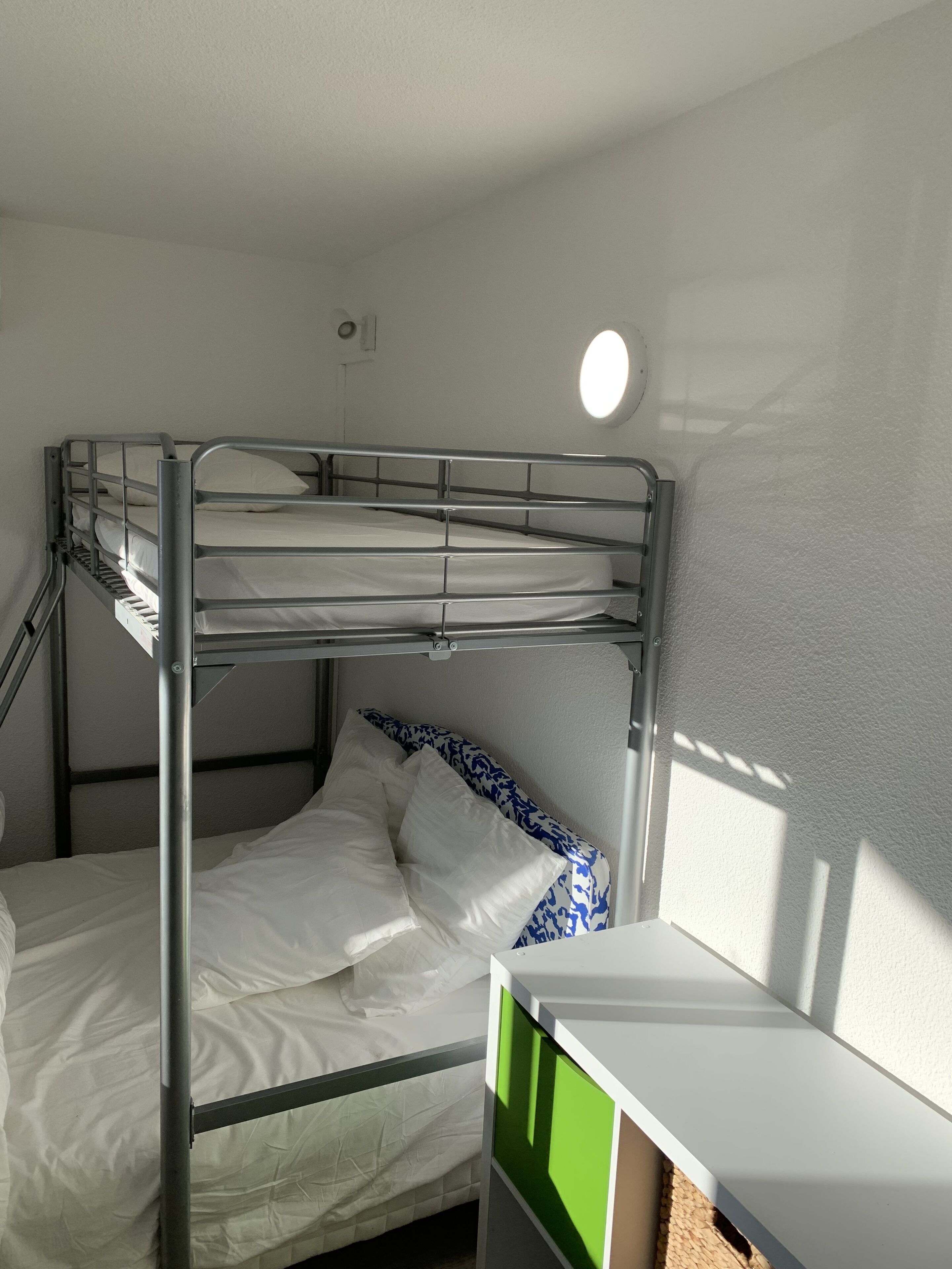 Un lit superposé avec une literie blanche et un meuble de rangement vert à côté.