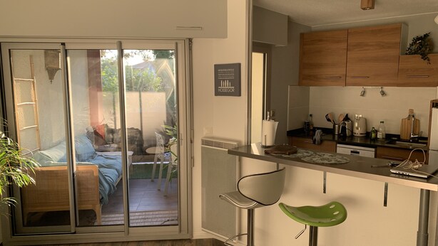 Une cuisine moderne avec des meubles en bois, un four encastré et un coin repas comprenant un tabouret de bar et une chaise.