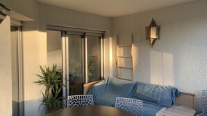 Une pièce chaleureuse avec une table en bois, un canapé bleu et une chaise blanche. Une porte-fenêtre coulissante donne accès à un balcon où se trouve une plante.