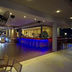 Zona de bar con barra, taburetes y área de estar con mesas y sillas.
