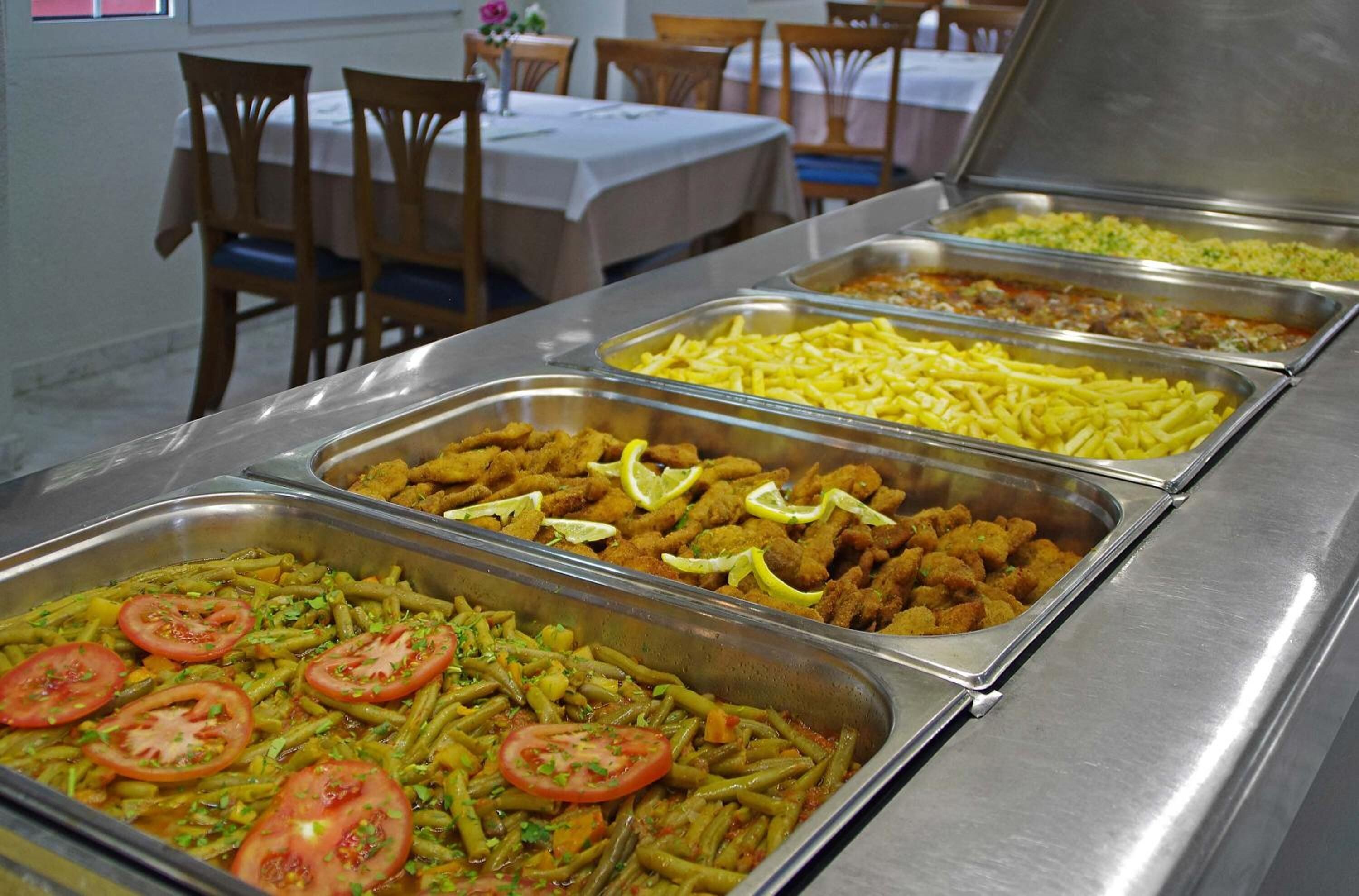 Un bufé con diversos platos, incluyendo opciones fritas, una ensalada y un guiso de verduras adornado con tomates.