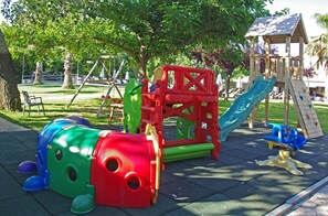 Une aire de jeux avec un toboggan, des structures d’escalade et un petit bâtiment.