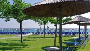Zona de playa con sombrillas de paja, sillas reclinables azules y una vista despejada del océano.
