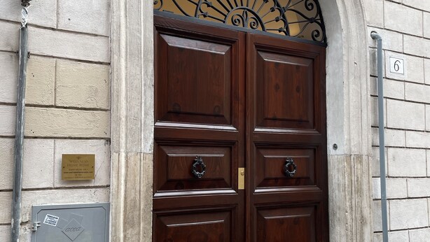Une porte en bois à deux battants, surmontée d’une arche décorative en métal, une boîte de raccordement électrique et une enseigne fixée au mur.