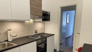 Une cuisine moderne avec des meubles blancs, un évier en acier inoxydable, une cuisinière à gaz et un four à micro-ondes.
