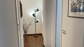 Un couloir avec un tapis à motifs, un lampadaire et une œuvre d’art encadrée accrochée au mur.