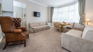 Un salon comprenant un fauteuil en cuir marron, un canapé beige et un coin repas avec une table et des chaises.