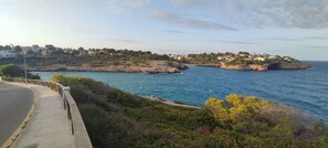 A coastal road with a sidewalk and a view of a rocky coastline with buildings on a hill. - Majorcan charm, with private pool and 100m from the beach. (CALA ROMANTICA)