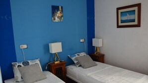 Ein Zimmer mit zwei Betten, jeweils mit weißer Matratze und passenden Kissen, und an beiden Seiten Nachttische mit Lampen.