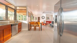A modern kitchen with wooden cabinets, a stainless steel refrigerator, and a dining area with a table and chairs.