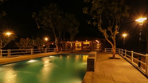 Zona de piscina al aire libre de noche con un edificio al fondo.