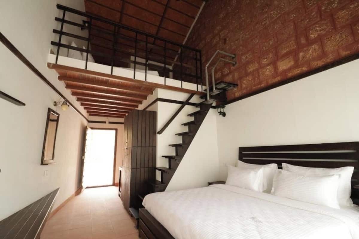 Quarto com uma cama grande, escada de madeira e vista para o exterior.