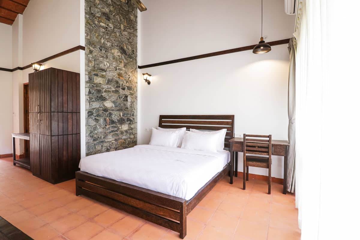 Quarto com cama de madeira, parede de pedra, escrivaninha com cadeira e guarda-roupa.