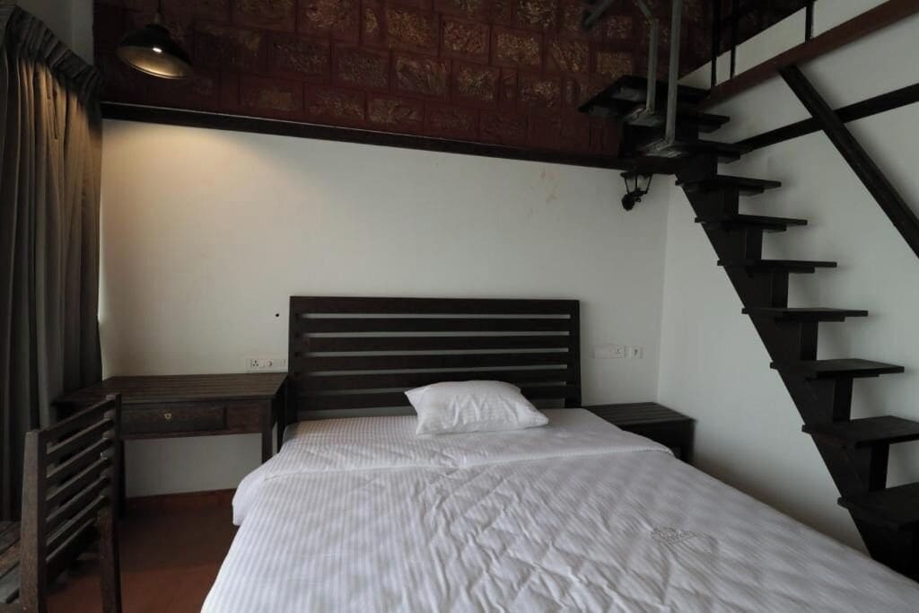 Quarto com cama de madeira, mesa de cabeceira, escrivaninha e escada.