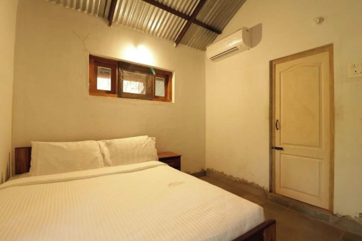 Quarto com cama, mesa de cabeceira de madeira, janela com vista, ar condicionado e porta.