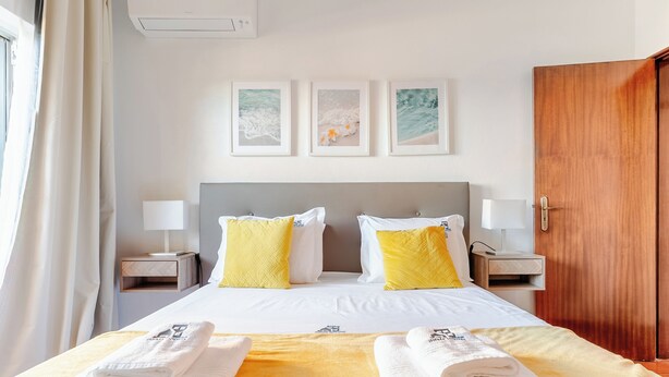 A hotel room with a bed, two bedside tables with lamps, a wooden wardrobe, and three framed pictures on the wall. - Ocean View • Walk to Beach • Pool • Lagos • 64 (Lagos)
