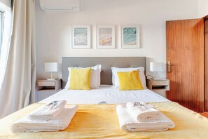 Habitación de hotel con cama, dos mesitas de noche con lámparas, un armario de madera y tres cuadros en la pared.