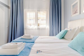 A hotel room with two beds, a large window, and a view of buildings outside. - Ocean View • Walk to Beach • Pool • Lagos • 64 (Lagos)
