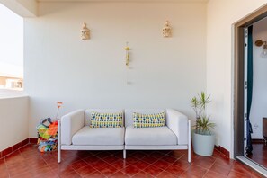 A white sofa with patterned cushions, a potted plant, and a small wind chime on a tiled floor. - Ocean View • Walk to Beach • Pool • Lagos • 64 (Lagos)