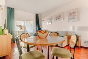 A dining area with a round wooden table, four chairs, a bowl of fruit, and a sofa with cushions. - Ocean View • Walk to Beach • Pool • Lagos • 64 (Lagos)