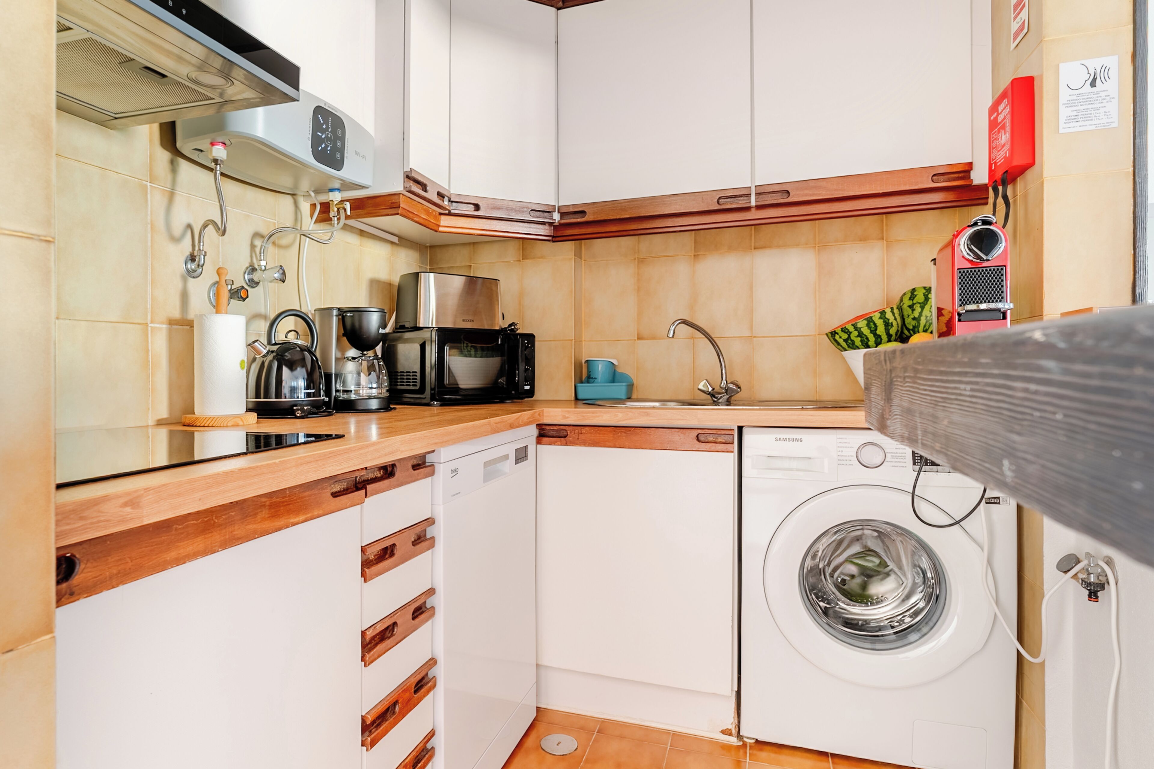Een kleine keuken met een wasmachine, een koffiezetapparaat en een magnetron.