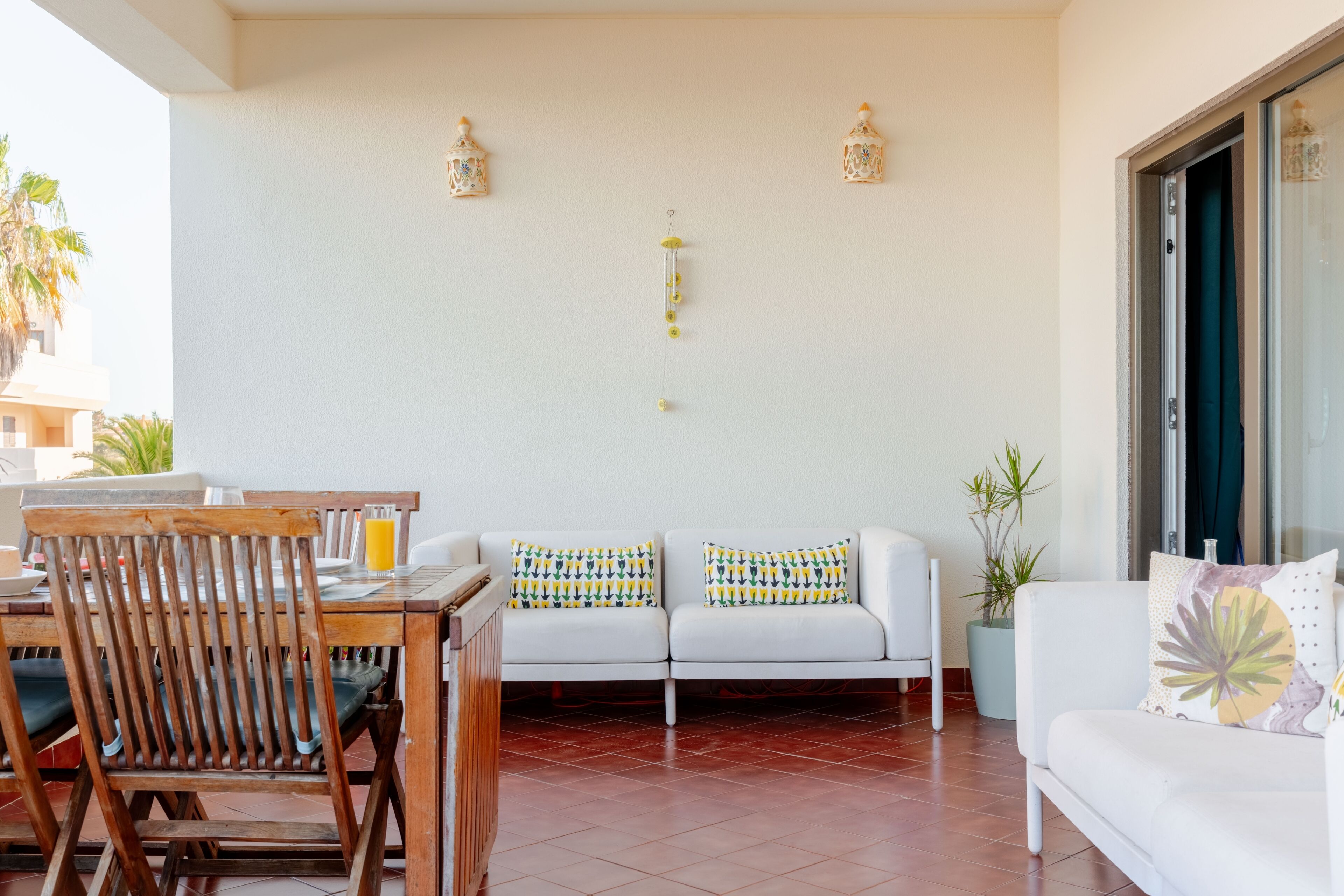 A living room with a white sofa, wooden chairs, a dining table, and a decorative wall with two hanging lanterns.