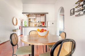 A dining area with a round table, four chairs, a bowl of fruit, and a kitchen in the background. - Ocean View • Walk to Beach • Pool • Lagos • 64 (Lagos)