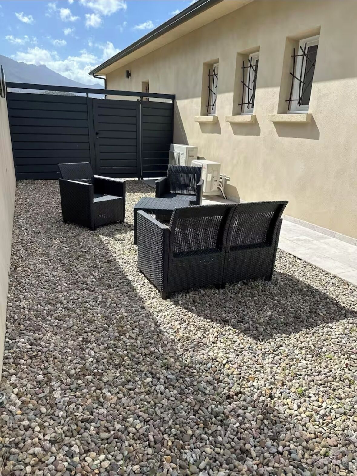 Un espace patio aménagé avec du mobilier d’extérieur, comprenant un canapé et des fauteuils, installé sur une surface de gravier.