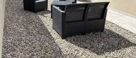 Un espace patio aménagé avec du mobilier d’extérieur, comprenant un canapé et des fauteuils, installé sur une surface de gravier.