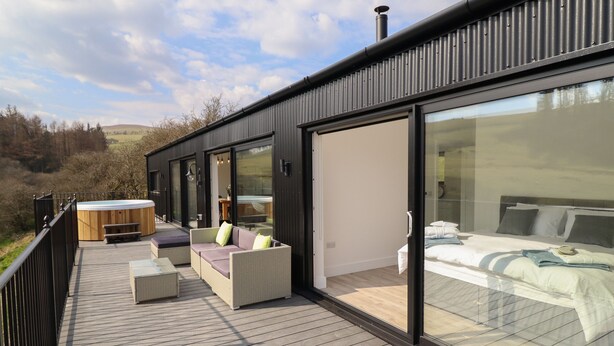 A modern outdoor deck with a hot tub, seating area, and a glass-enclosed bedroom. - The Sheep Shed (Oswestry)