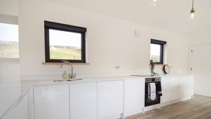 A modern kitchen with white cabinets, a built-in oven, and a window overlooking a grassy area. - The Sheep Shed (Oswestry)