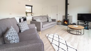 A modern living room with a sofa, a coffee table, a fireplace, and a television. - The Sheep Shed (Oswestry)