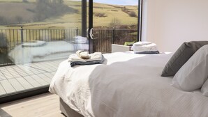 A bedroom with a large window, a bed with white linens, and a view of a landscape. - The Sheep Shed (Oswestry)
