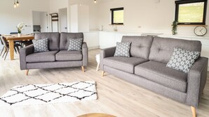 A modern living room with two grey sofas, a wooden dining table, and a kitchen in the background. - The Sheep Shed (Oswestry)
