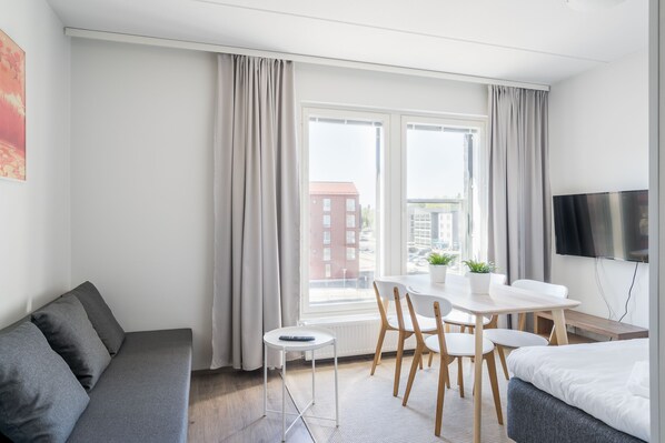 Une chambre d’hôtel moderne équipée d’un canapé, d’une table à manger avec des chaises, d’un lit, d’une télévision et d’une fenêtre avec des rideaux.