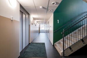 Un couloir d’hôtel moderne avec un mur végétal, un escalier et une entrée recouverte de moquette.