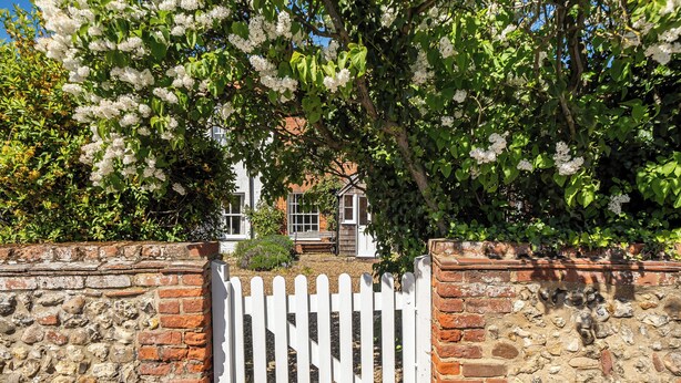 Un mur de pierres surmonté d’une clôture en bois peinte en blanc, un mur de briques et un arbre aux fleurs blanches.
